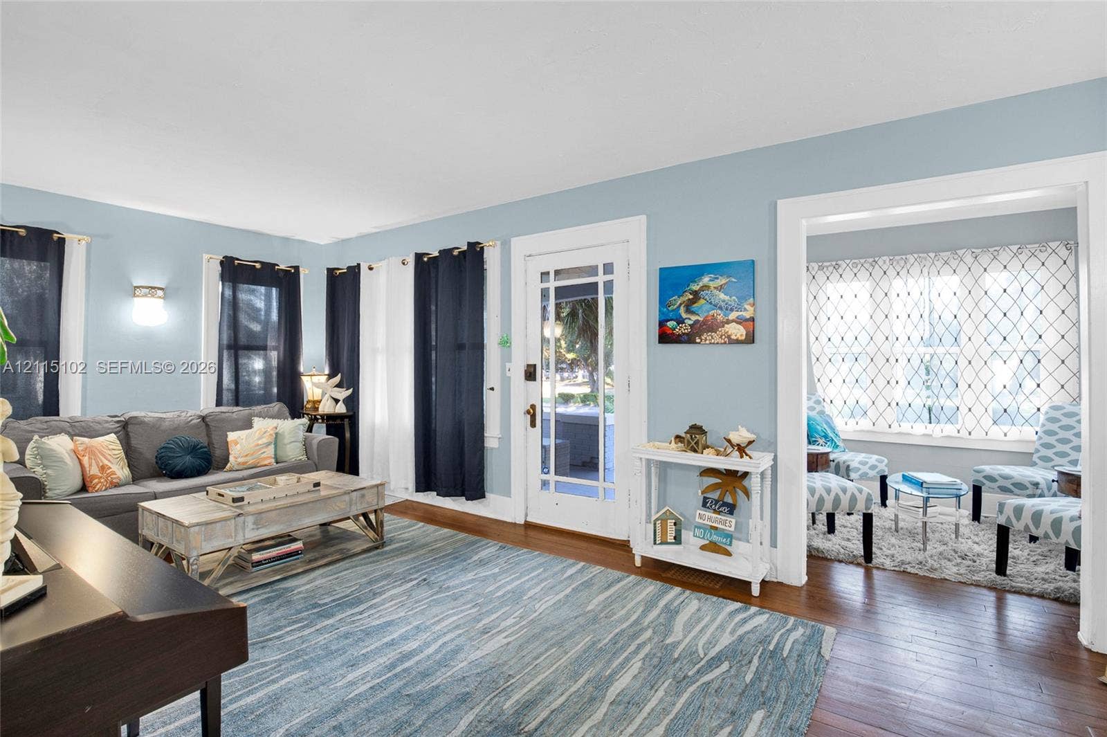 110 S Peninsula, New Smyrna Beach, FL 32169 Living area featuring wood-finish flooring, a multi-pane glass entry door, and an archway leading to a secondary room with decorative lattice window film and wall-mounted lighting