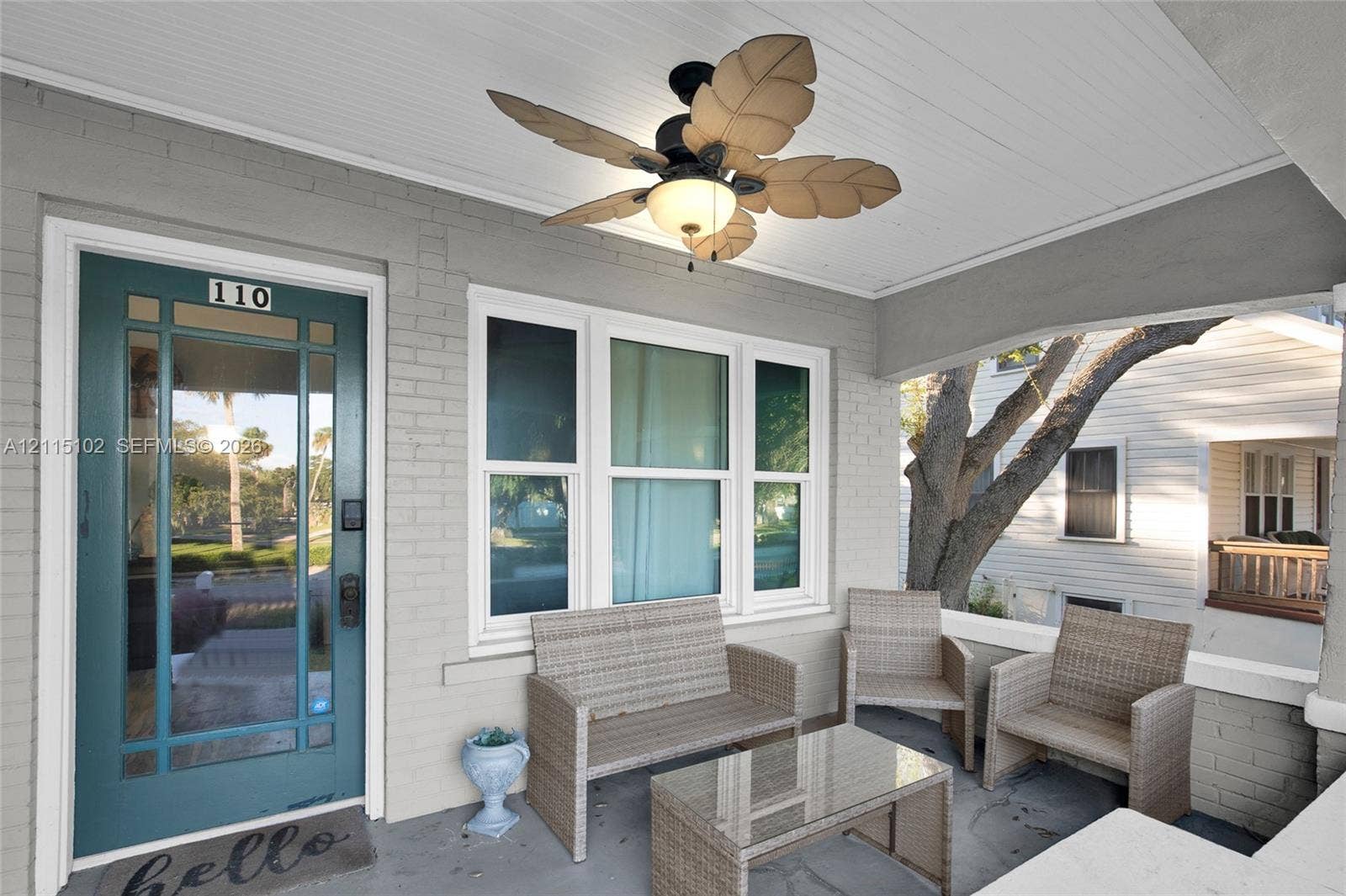 110 S Peninsula, New Smyrna Beach, FL 32169 Covered front porch featuring a painted brick exterior, teal-finished glass-paneled entry door, beadboard ceiling, and integrated palm-leaf style ceiling fan