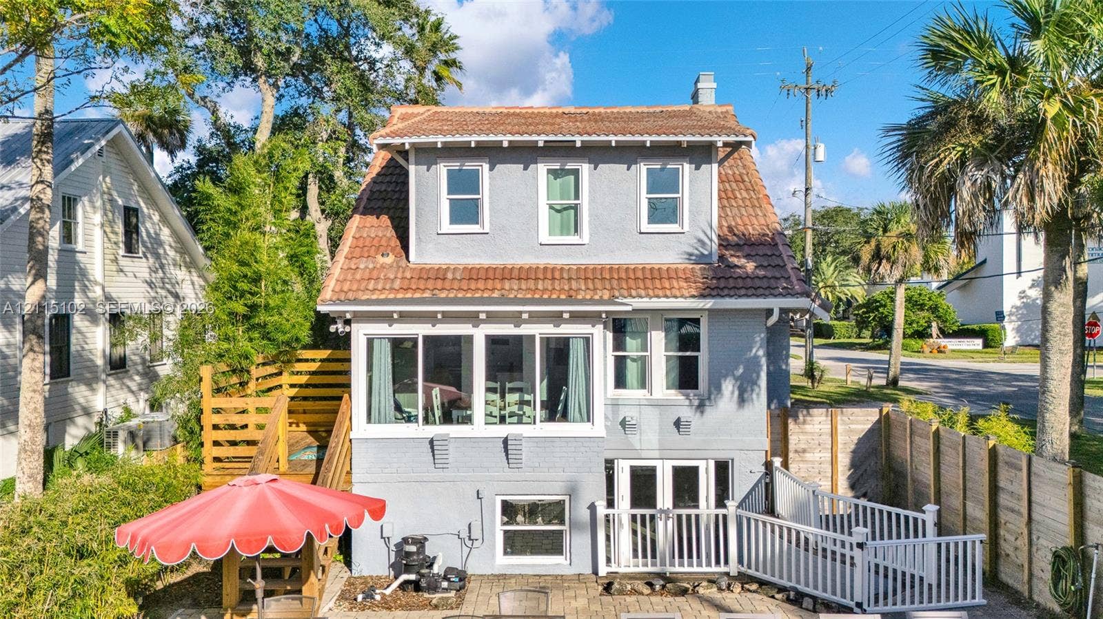 110 S Peninsula, New Smyrna Beach, FL 32169 Multi-level exterior featuring a mansard roof, stucco siding, a glass-enclosed upper porch, and a paved ground-level patio with decorative fencing