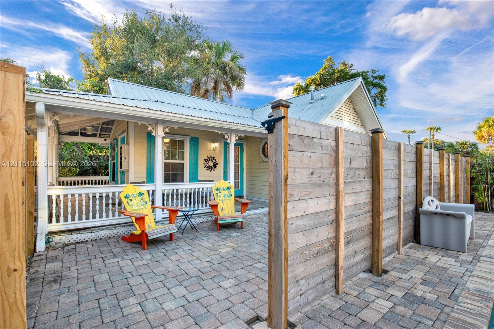 110 S Peninsula, New Smyrna Beach, FL 32169 Paver patio area featuring a horizontal wood-plank privacy fence and a covered porch with decorative corbels and white balustrade railing