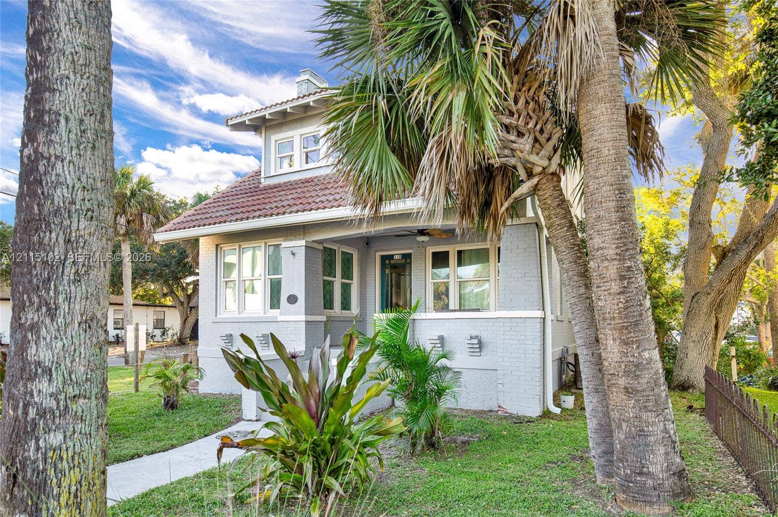 110 S Peninsula, New Smyrna Beach, FL 32169 Craftsman-style exterior featuring a painted brick facade, a covered front porch, and a tiled roof, set within a landscaped yard