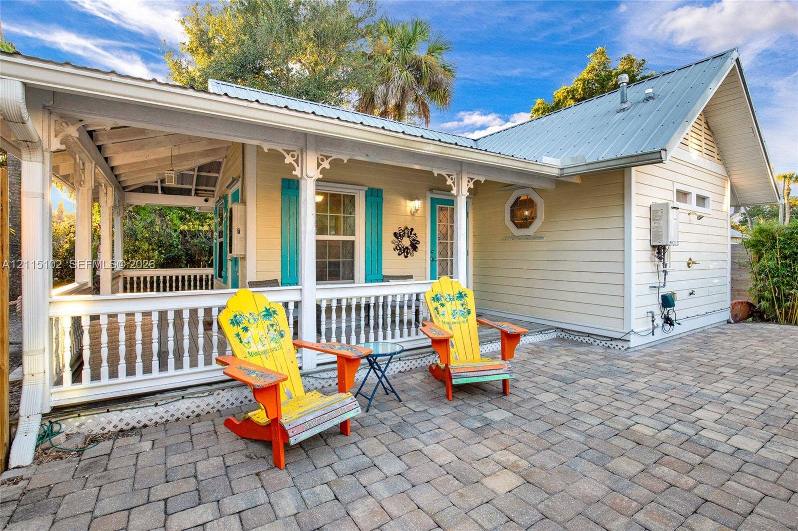 110 S Peninsula, New Smyrna Beach, FL 32169 Covered wrap-around porch with decorative millwork, light-colored horizontal siding, metal roofing, and stone paver patio