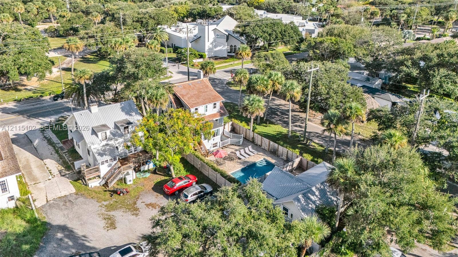110 S Peninsula, New Smyrna Beach, FL 32169 Aerial perspective featuring an in-ground swimming pool, wood fencing, multiple structures with metal roofing, and mature palm trees