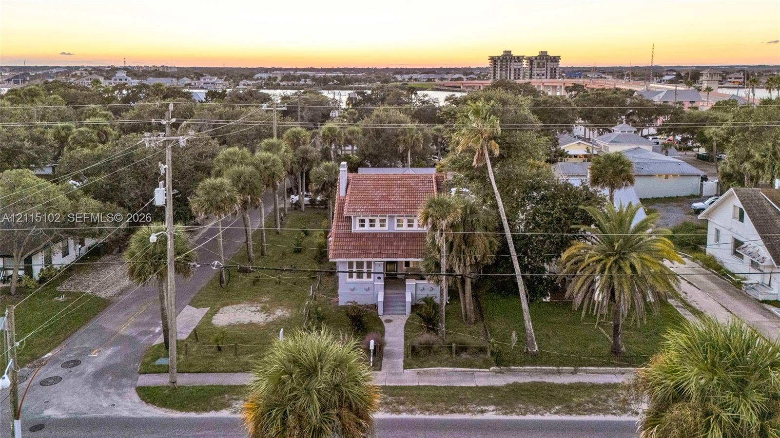110 S Peninsula, New Smyrna Beach, FL 32169 Two-story residence featuring a tile roof, light-toned exterior finish, prominent front-facing gable, and mature palm landscaping