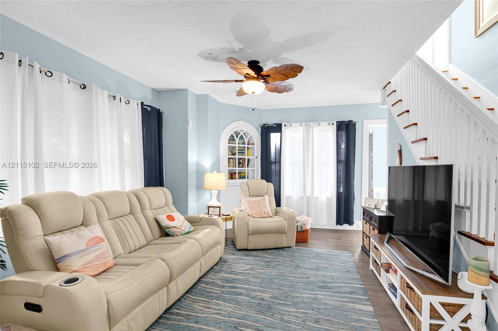 110 S Peninsula, New Smyrna Beach, FL 32169 Living area featuring wood-finish flooring, a ceiling fan with leaf-shaped blades, arched built-in shelving, and a staircase with white balusters
