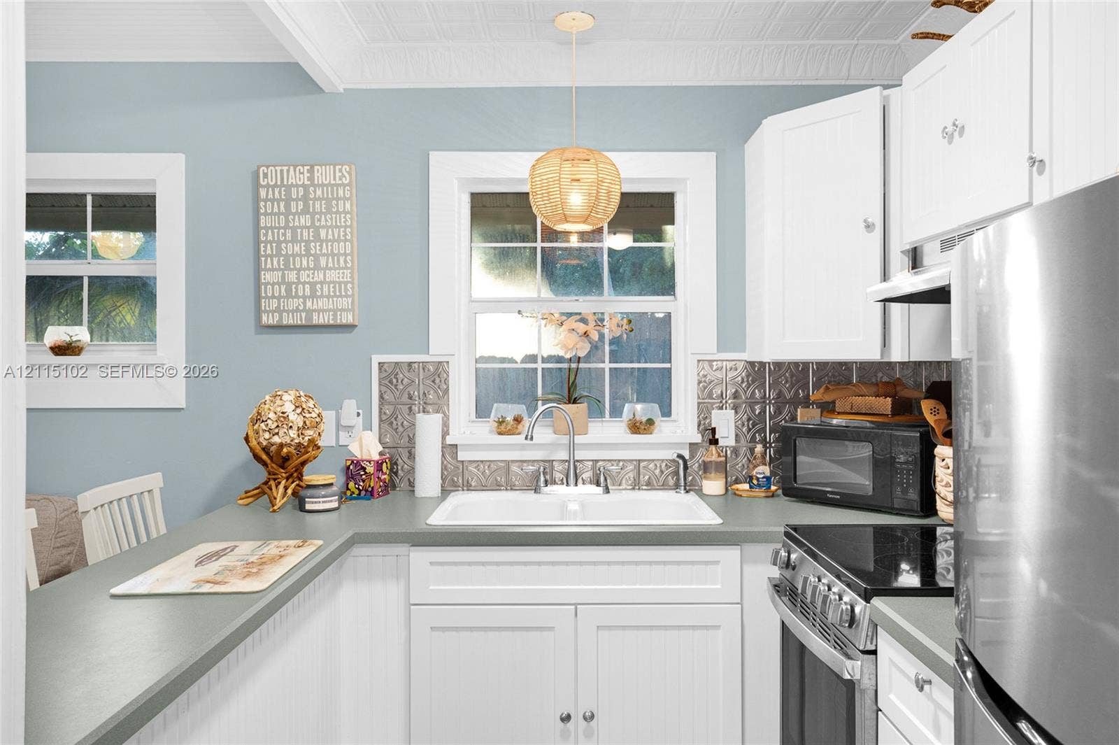 110 S Peninsula, New Smyrna Beach, FL 32169 Kitchen featuring white beadboard cabinetry, metallic decorative backsplash, double-basin sink with gooseneck faucet, textured ceiling, and pendant lighting