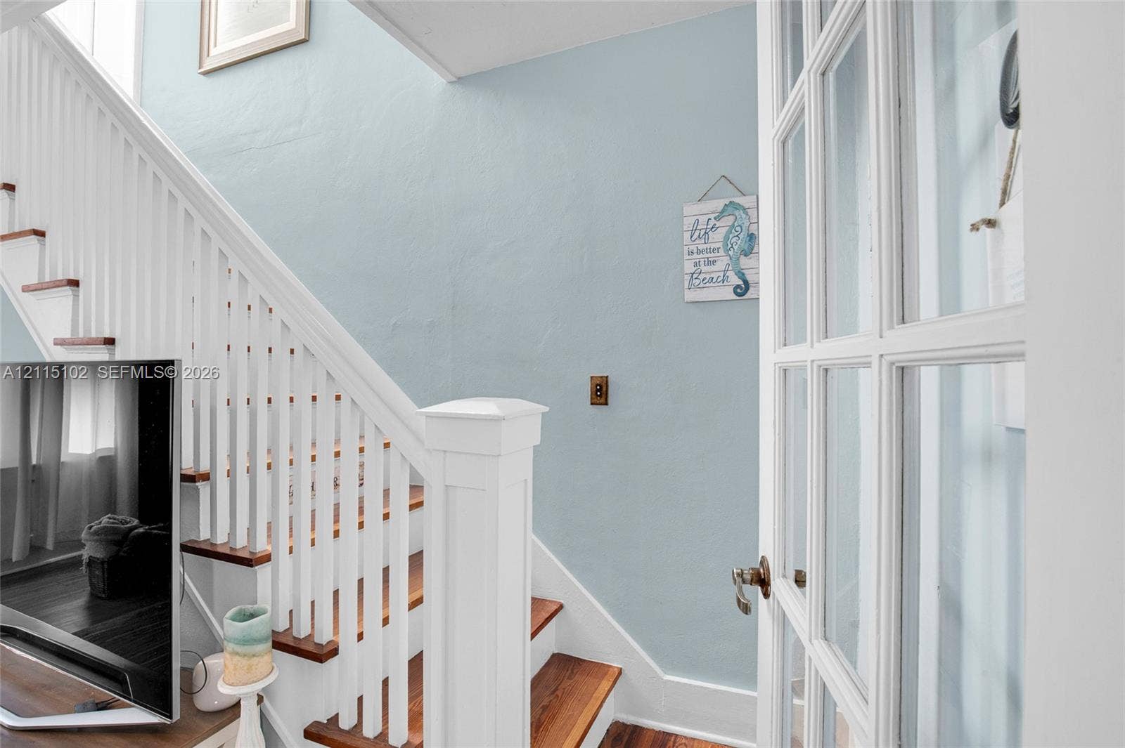 110 S Peninsula, New Smyrna Beach, FL 32169 Staircase featuring wood-finish treads, a white balustrade with a prominent newel post, and an attached multi-pane French door
