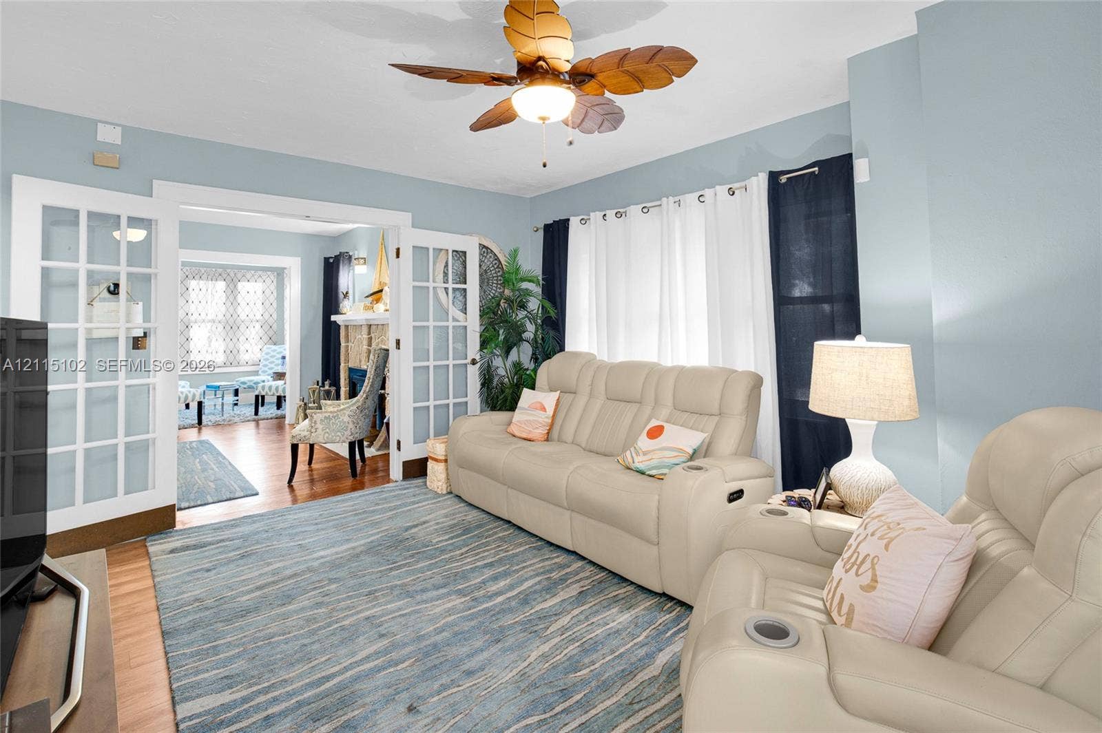 110 S Peninsula, New Smyrna Beach, FL 32169 Interior space featuring double French doors, wood-finish flooring, a decorative ceiling fan with integrated lighting, and a fireplace with textured masonry surround