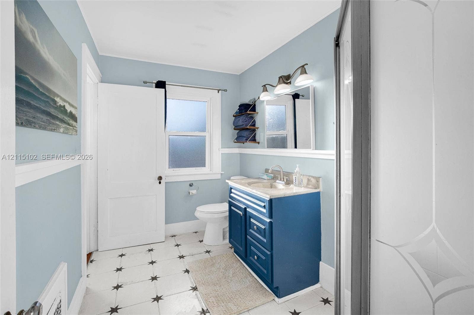 110 S Peninsula, New Smyrna Beach, FL 32169 Bathroom featuring a blue vanity with a stone countertop, a single-handle faucet, a three-light fixture, and patterned tile flooring