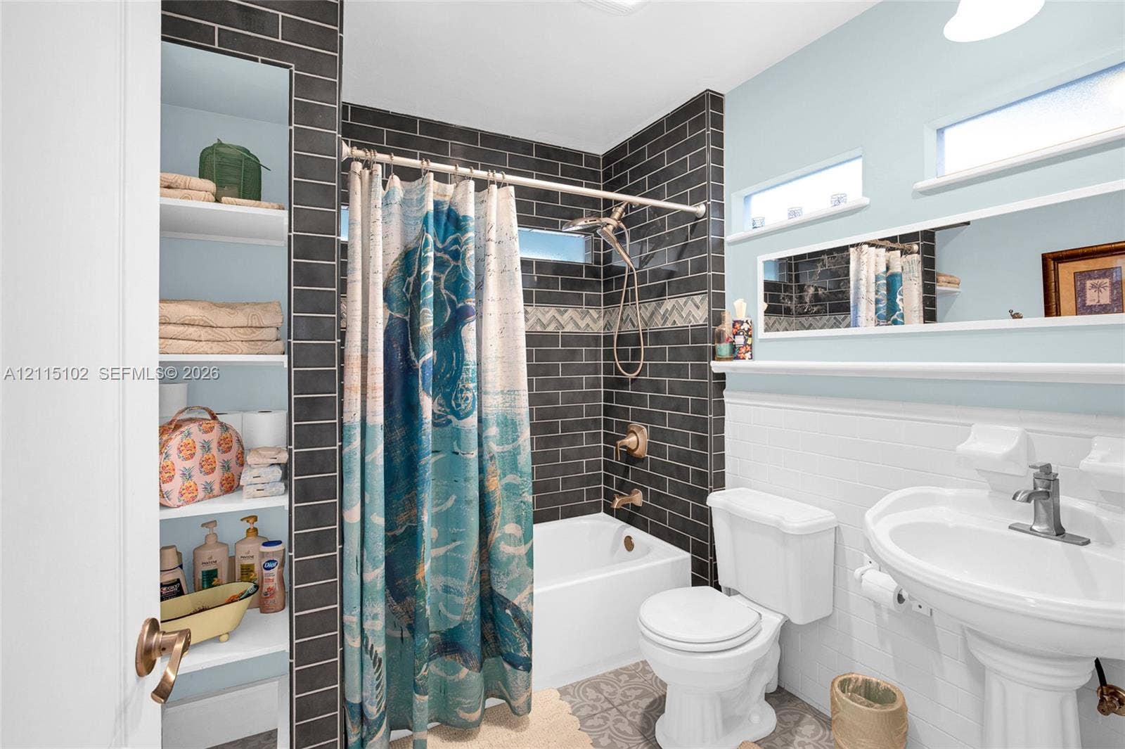 110 S Peninsula, New Smyrna Beach, FL 32169 Bathroom featuring charcoal subway tile surround, integrated floor-to-ceiling built-in shelving, pedestal sink with polished metal faucet, white subway tile wainscoting, and upper horizontal windows