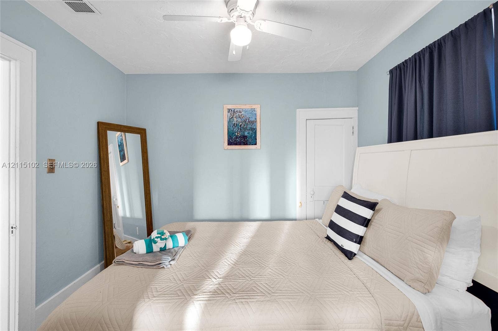 110 S Peninsula, New Smyrna Beach, FL 32169 Bedroom featuring light blue walls, a white ceiling fan with integrated lighting, and a white five-panel interior door