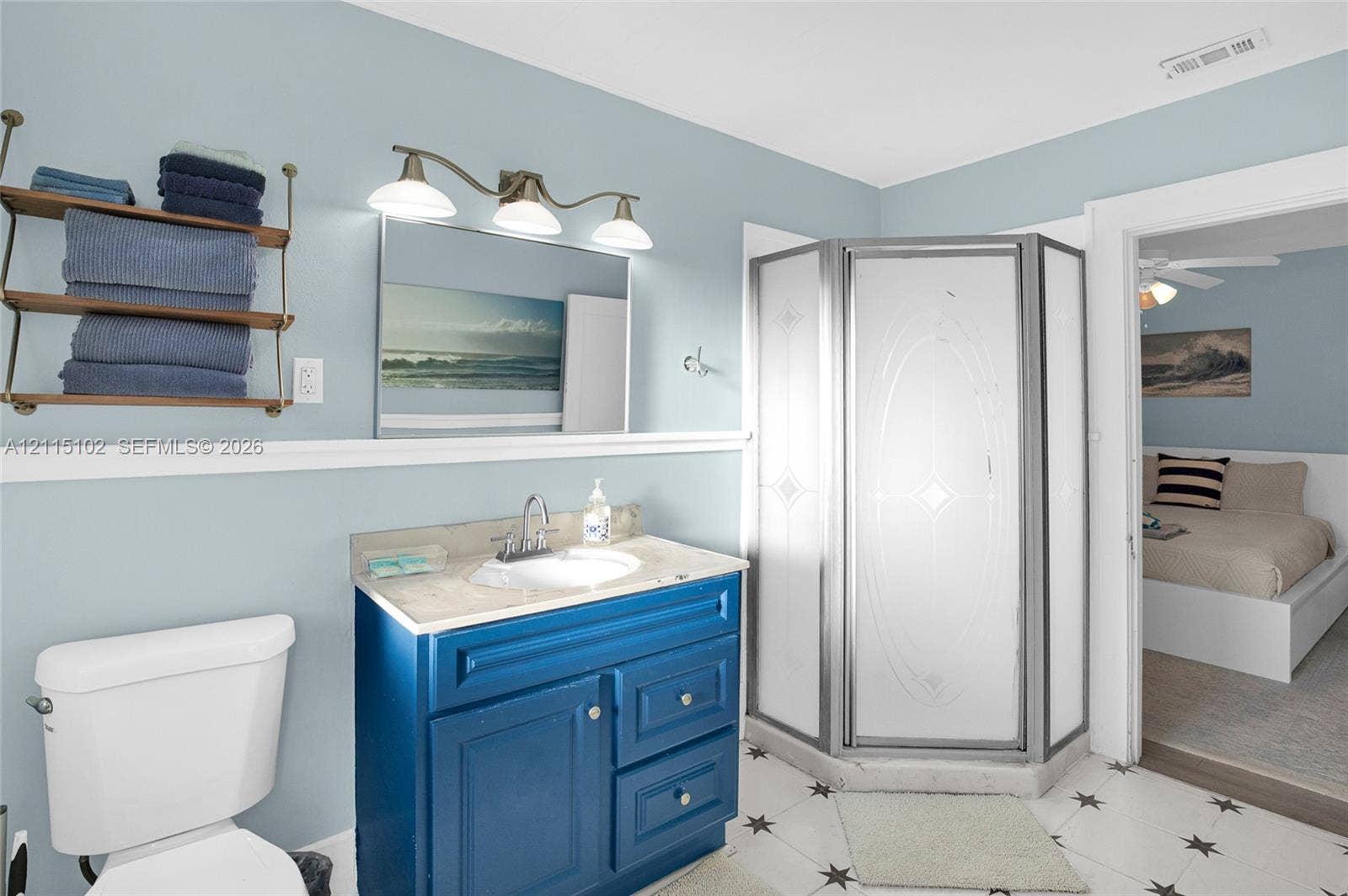 110 S Peninsula, New Smyrna Beach, FL 32169 Bathroom featuring a vanity with integrated sink and stone-finish countertop, corner shower enclosure with patterned glass, wall-mounted shelving unit, and three-light fixture