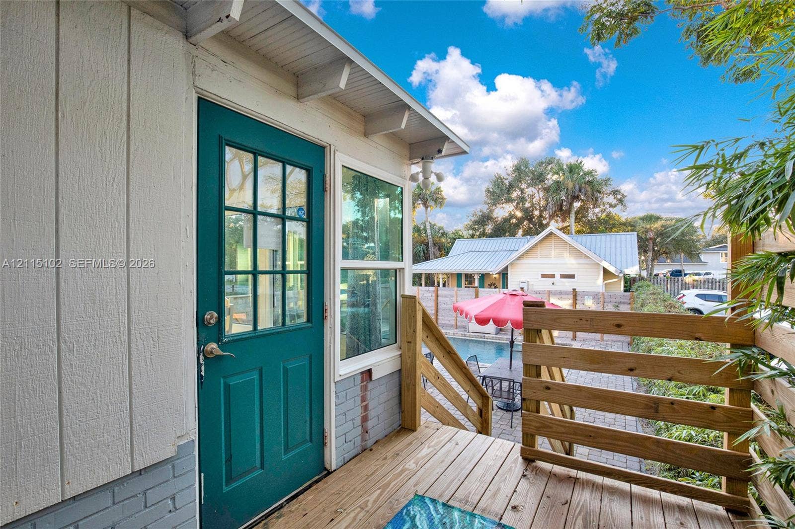 110 S Peninsula, New Smyrna Beach, FL 32169 Exterior deck featuring horizontal wood railings, teal-painted door with grid window, paneled siding, and a brick base