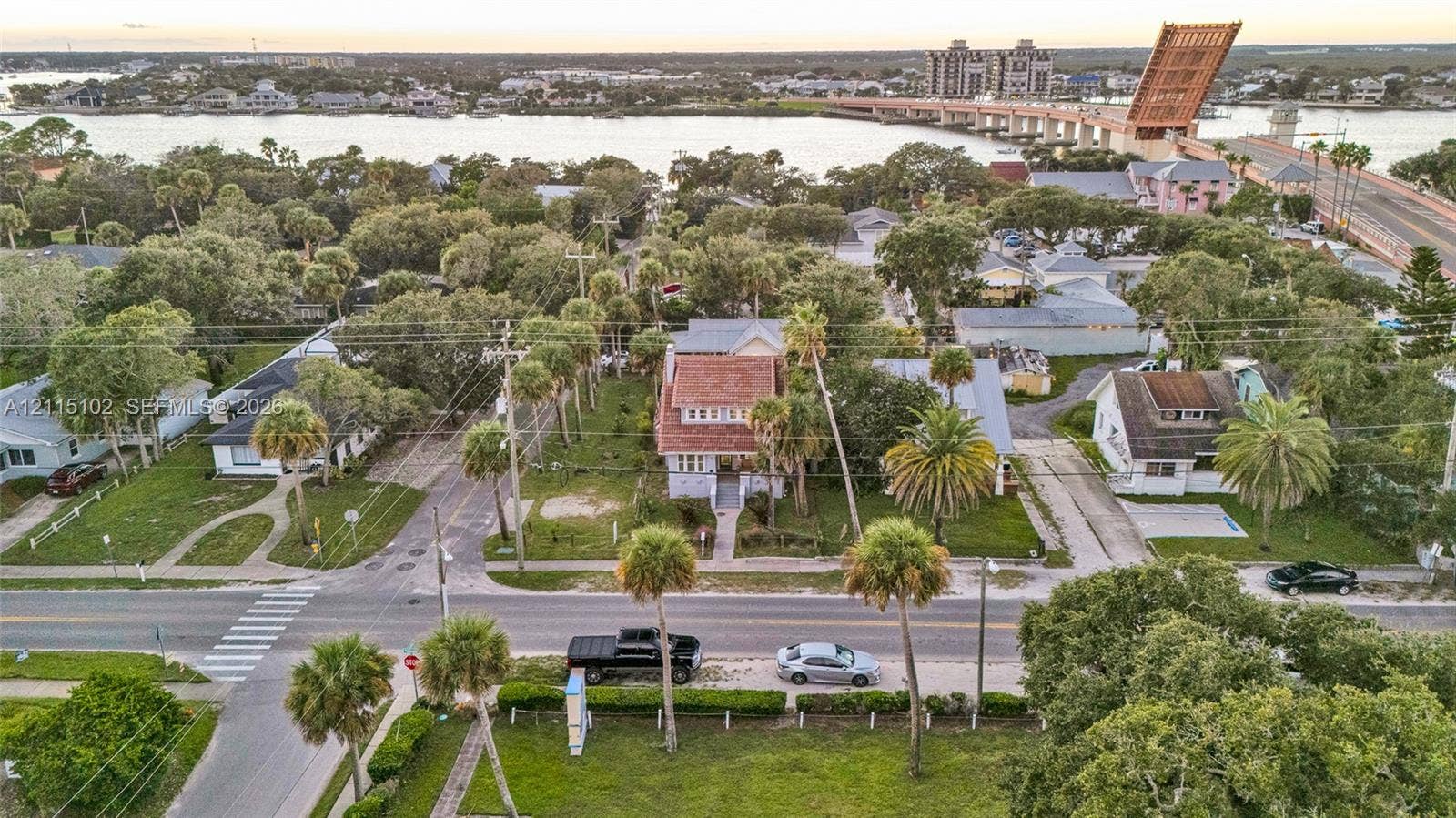 110 S Peninsula, New Smyrna Beach, FL 32169 Aerial perspective featuring a multi-story residence with a pitched tile roof, situated in a coastal area with mature palms and proximate to a waterway and bridge
