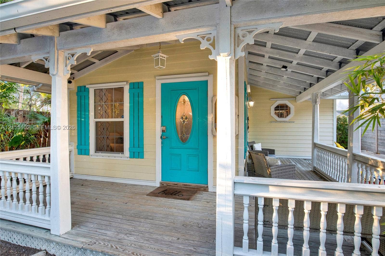 110 S Peninsula, New Smyrna Beach, FL 32169 Covered wraparound porch featuring white spindle railings, decorative wooden brackets, horizontal lap siding, and a prominent entryway with a glass-inset door and contrasting shutters