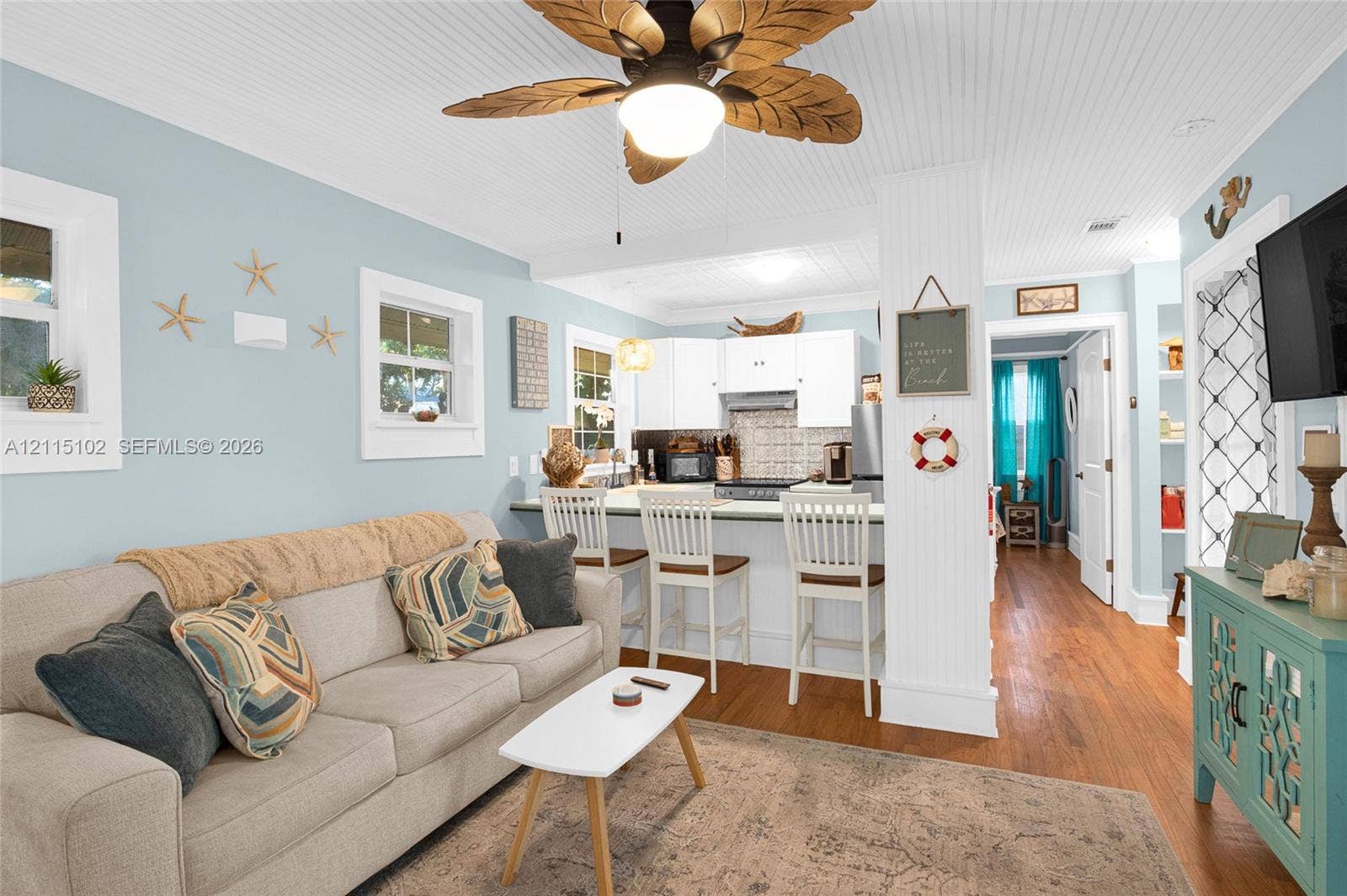 110 S Peninsula, New Smyrna Beach, FL 32169 Open-concept living space featuring wood-finish flooring, beadboard ceiling detail, integrated breakfast bar with white cabinetry, and palm-leaf ceiling fan
