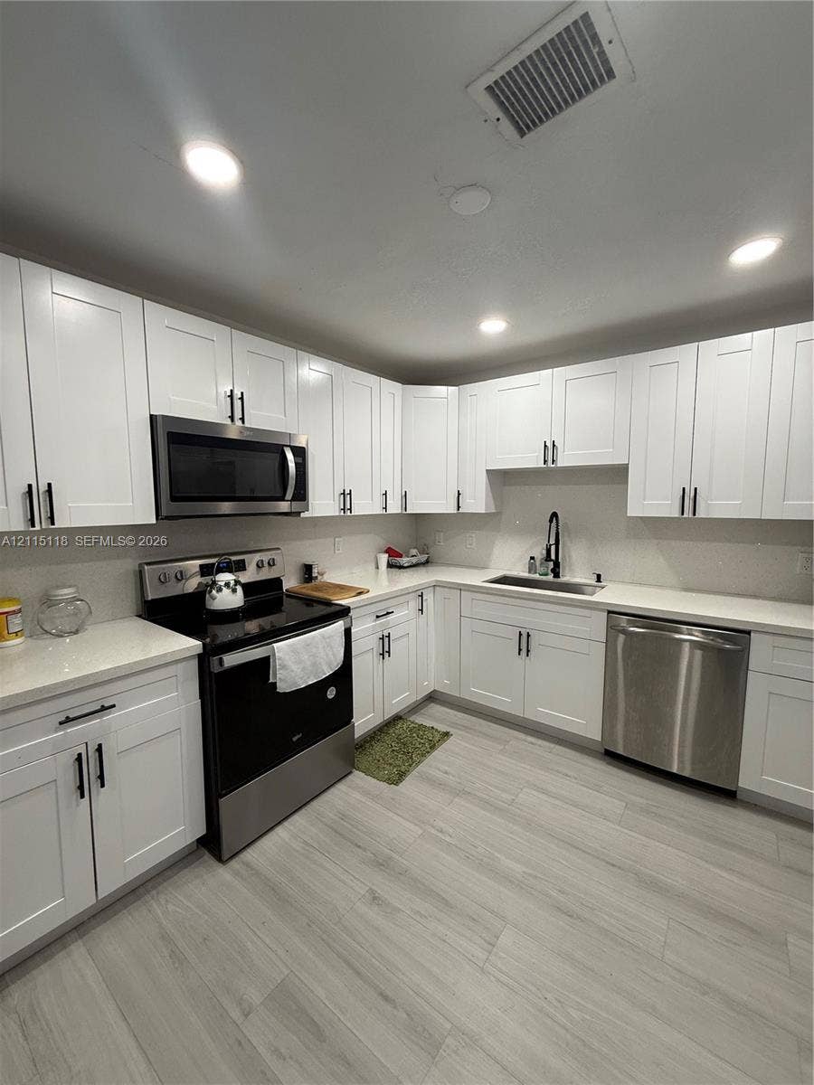 2816 SW 4th Place, #A, Fort Lauderdale, Fort Lauderdale, FL 33312 Kitchen featuring white Shaker-style cabinetry, stainless steel appliances, light-toned countertops, a stainless steel undermount sink with a matte black faucet, and wood-finish flooring