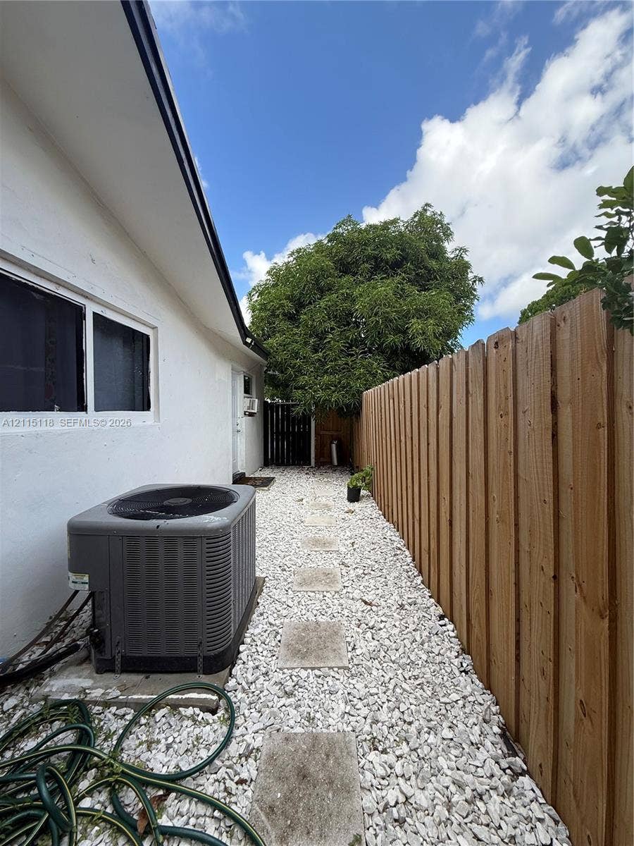 2816 SW 4th Place, #A, Fort Lauderdale, Fort Lauderdale, FL 33312 Side yard exterior featuring a vertical wood privacy fence, white stone ground cover, stone pavers, and a mounted central air conditioning unit