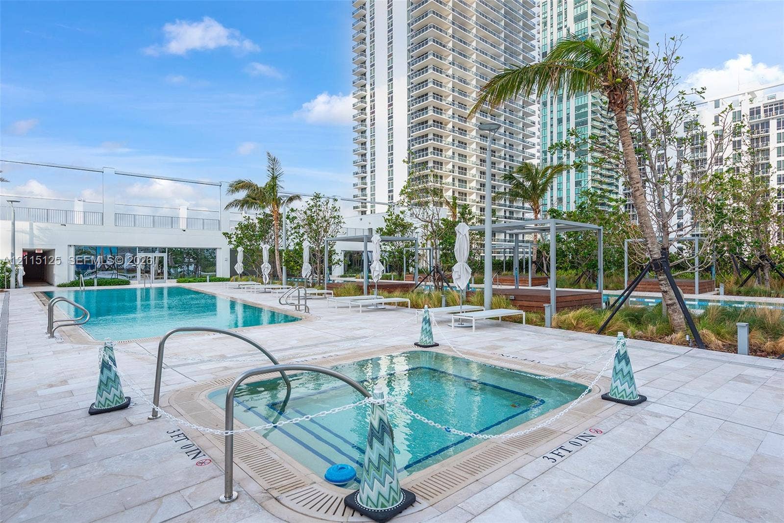 Swimming pool and spa area featuring natural stone deck surfacing, integrated metal handrails, and surrounding palm tree landscaping