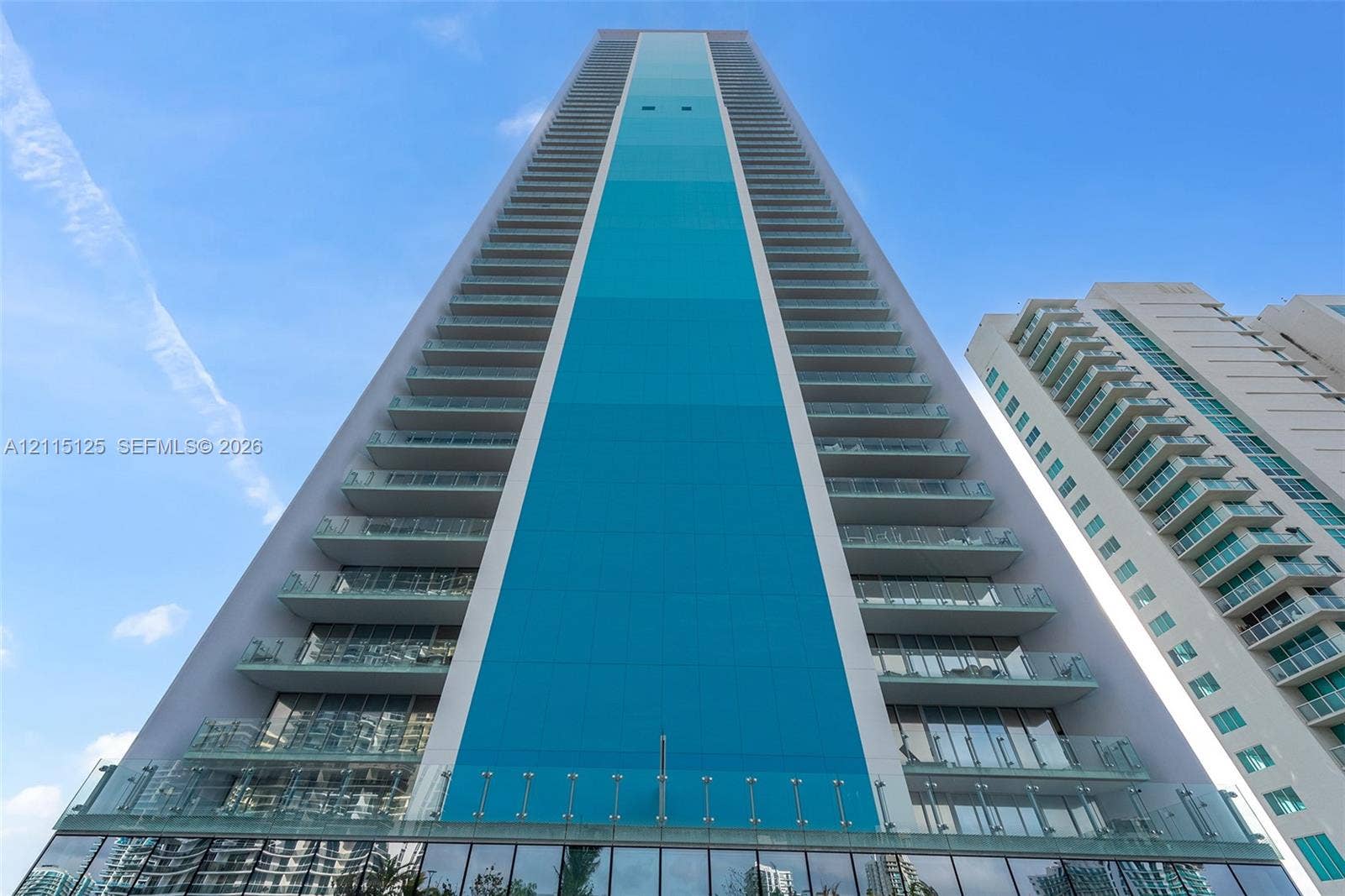 High-rise exterior featuring a striking turquoise accent panel, floor-to-ceiling glass windows, and private glass-railed balconies