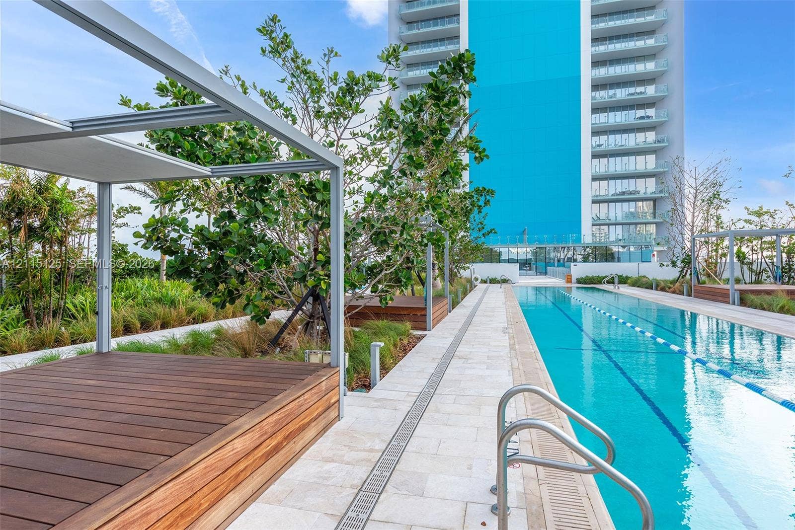 Lap pool with lane markers, natural stone decking, elevated wood-finish platforms, metal pergola structures, and integrated landscaping