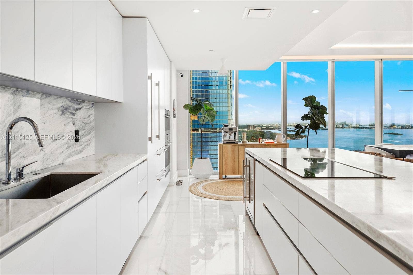Modern kitchen featuring floor-to-ceiling white cabinetry, stone slab countertops and backsplash, integrated cooktop, and expansive wall-to-wall windows
