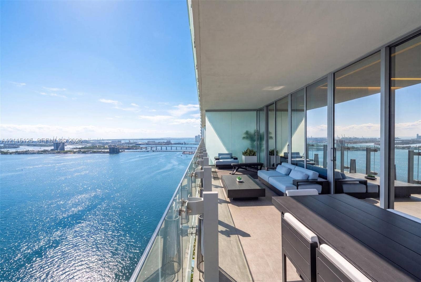 Expansive covered balcony featuring floor-to-ceiling glass doors, a glass panel railing, and water frontage