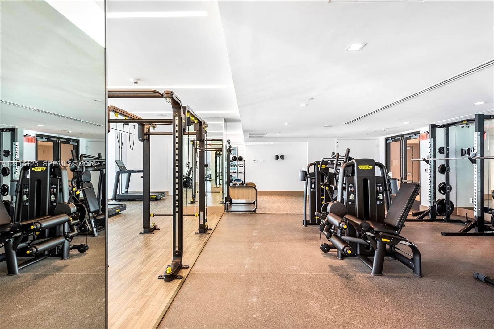 Fitness center featuring recessed ceiling lighting, wall-to-wall mirrors, and a combination of wood-finish and resilient rubberized flooring