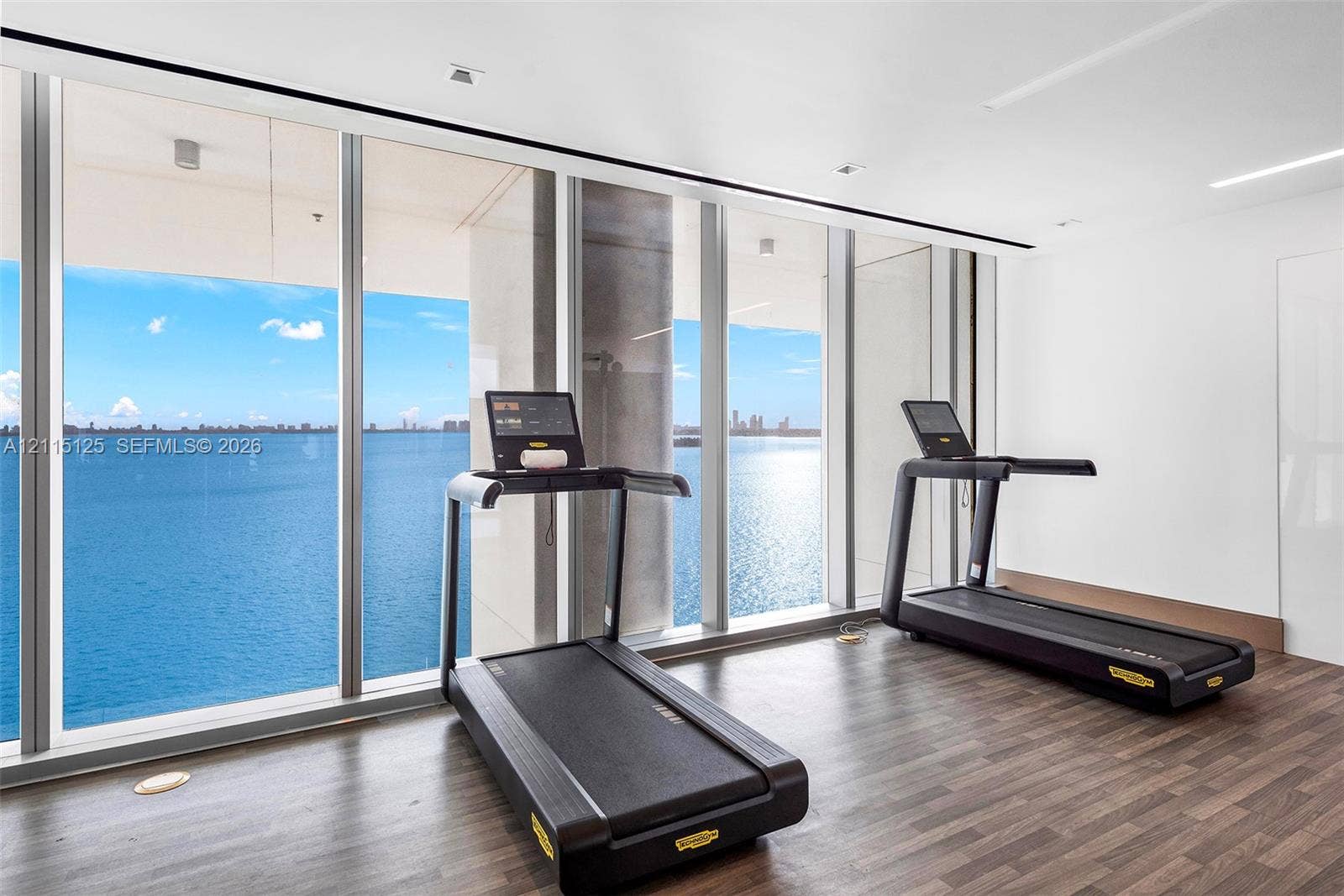 Floor-to-ceiling windows, wood-finish flooring, and expansive water backdrop