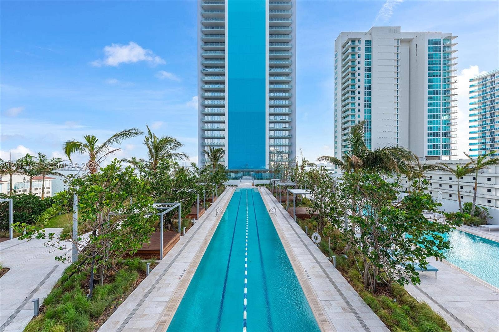 Linear lap pool with lane markers, surrounded by stone-tile decking, manicured landscaping, and mature palms