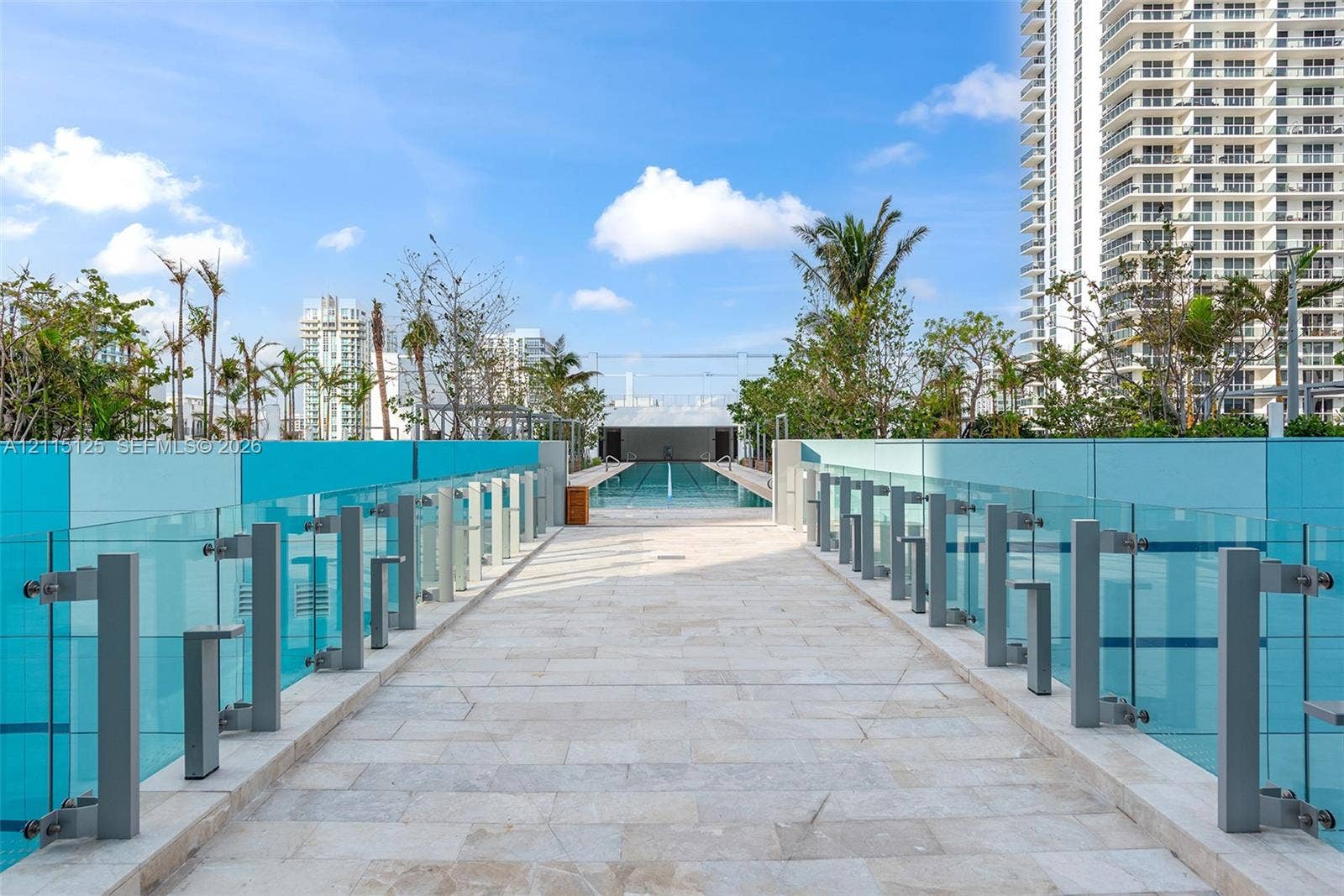 Elevated stone-paved promenade featuring glass panel railings, integrated pathway lighting, and lap pool access