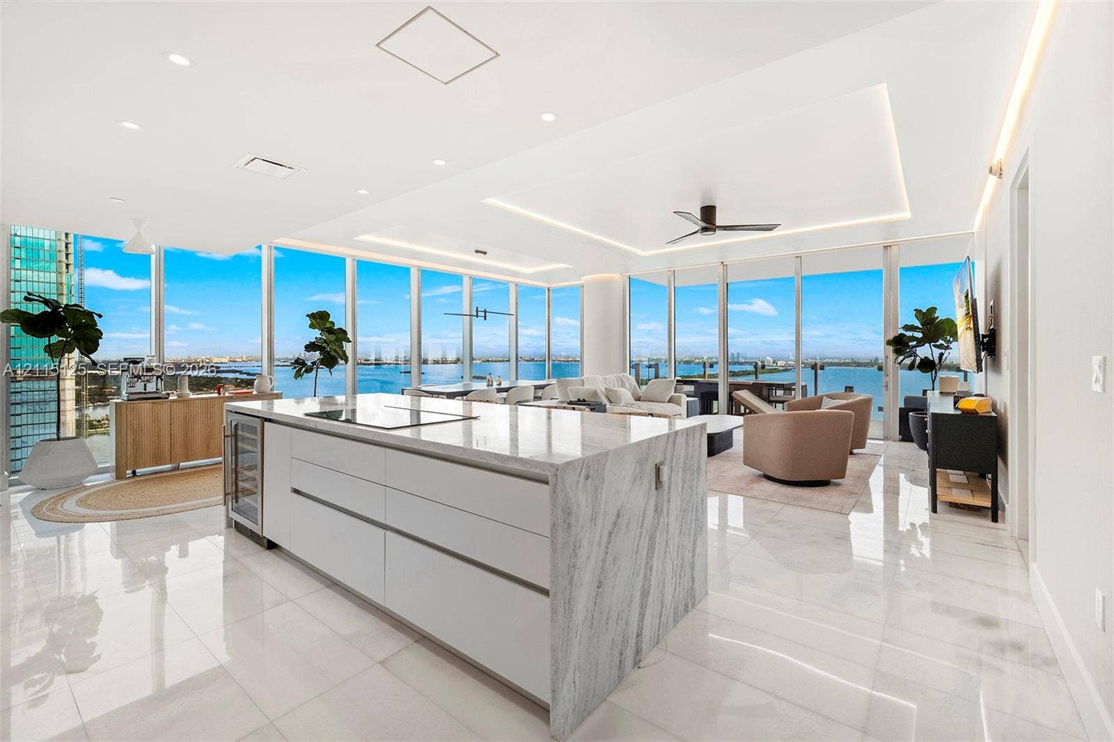 Open-concept kitchen featuring an oversized stone-topped island, flat-panel cabinetry, built-in wine refrigeration, floor-to-ceiling glass windows, and polished stone flooring