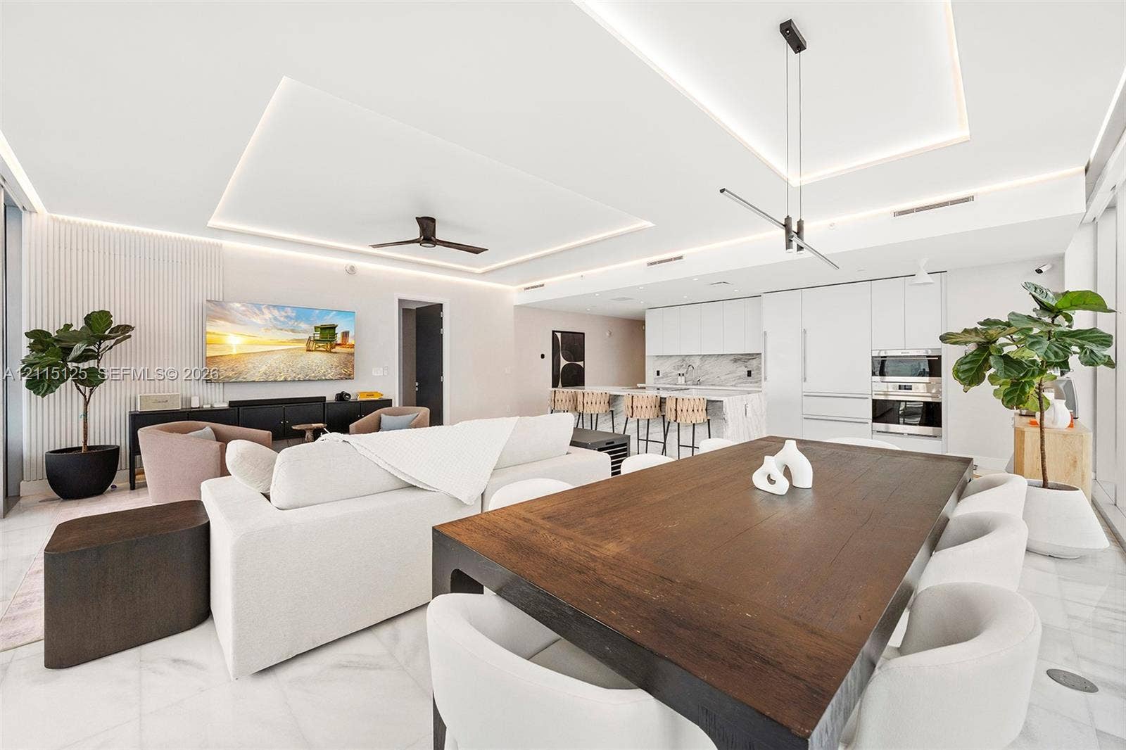Open-concept interior featuring high ceilings with recessed LED perimeter lighting, flat-panel cabinetry, built-in stainless steel double ovens, and polished stone flooring