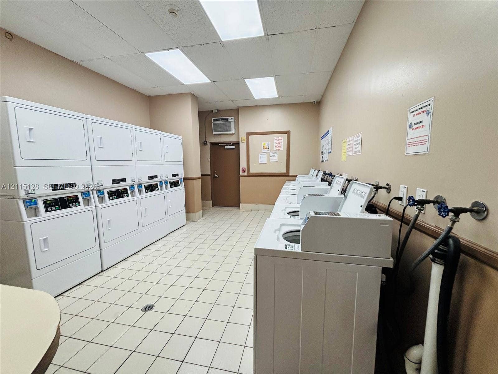 1817 S Ocean Drive, #426, Hallandale Beach, FL 33009 Laundry facility featuring multiple stacked washer-dryer units, high-capacity top-loading washing machines, ceramic tile flooring, and drop ceiling lighting