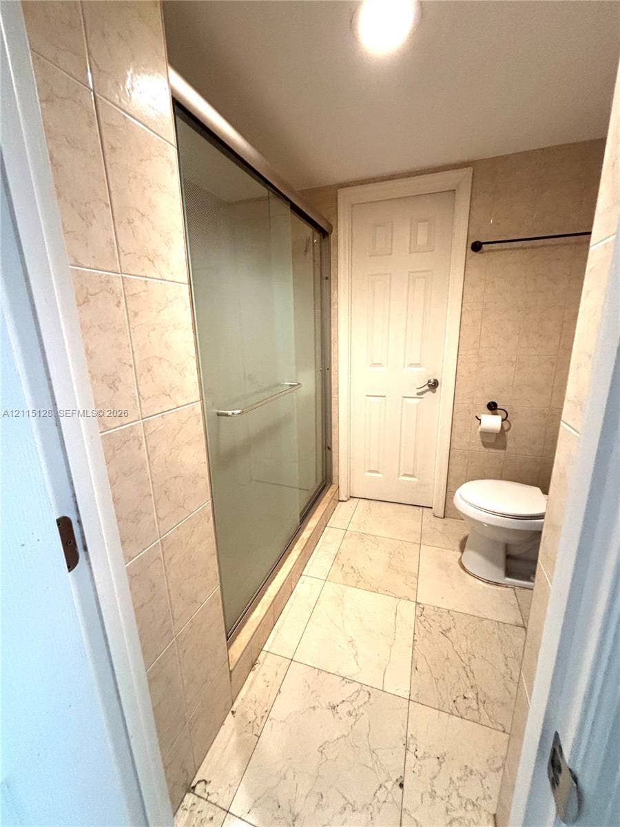 1817 S Ocean Drive, #426, Hallandale Beach, FL 33009 Walk-in shower with sliding glass doors, large-format tile flooring, neutral wall tiling, and a white interior door