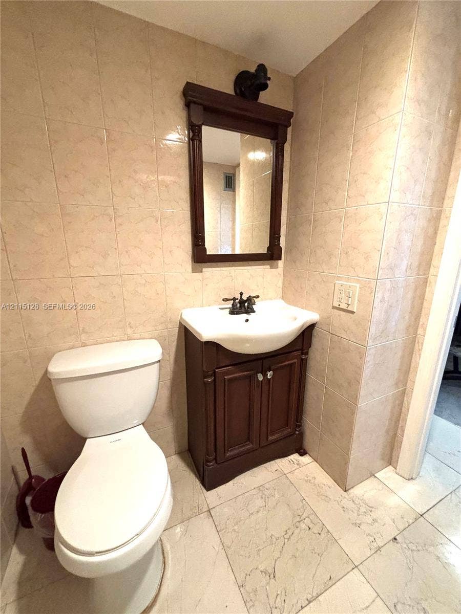 1817 S Ocean Drive, #426, Hallandale Beach, FL 33009 Bathroom featuring tile wall surround, vanity cabinet with a porcelain sink, dual-handle faucet, and framed wall-mounted mirror
