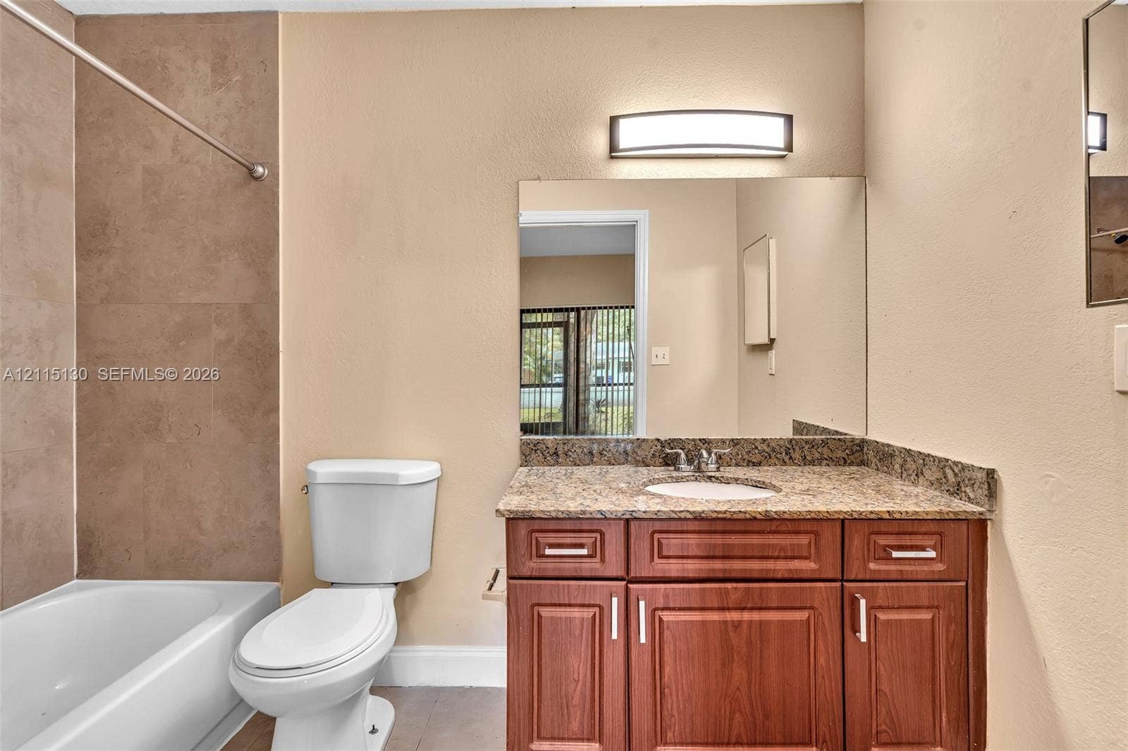 2445 SW 18th Terrace, #412, Fort Lauderdale, FL 33315 Bathroom featuring a vanity with wood-finish cabinetry, stone countertop, integrated sink, and wall-mounted light fixture, paired with a shower and tub combination featuring ceramic wall tile