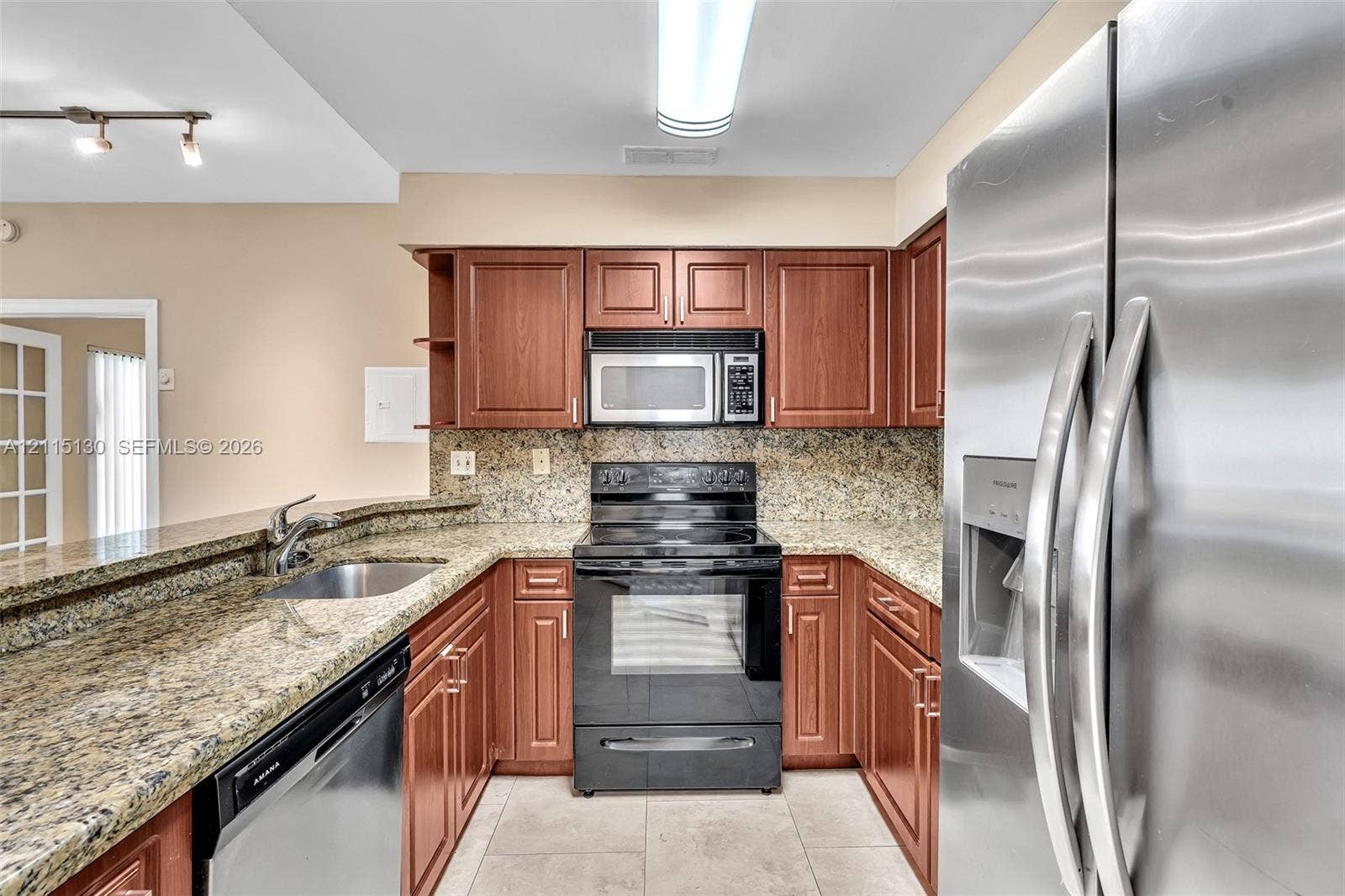 2445 SW 18th Terrace, #412, Fort Lauderdale, FL 33315 Kitchen featuring warm-tone cabinetry, stone-finish countertops, stainless steel appliances, and a double-basin undermount sink with a gooseneck faucet
