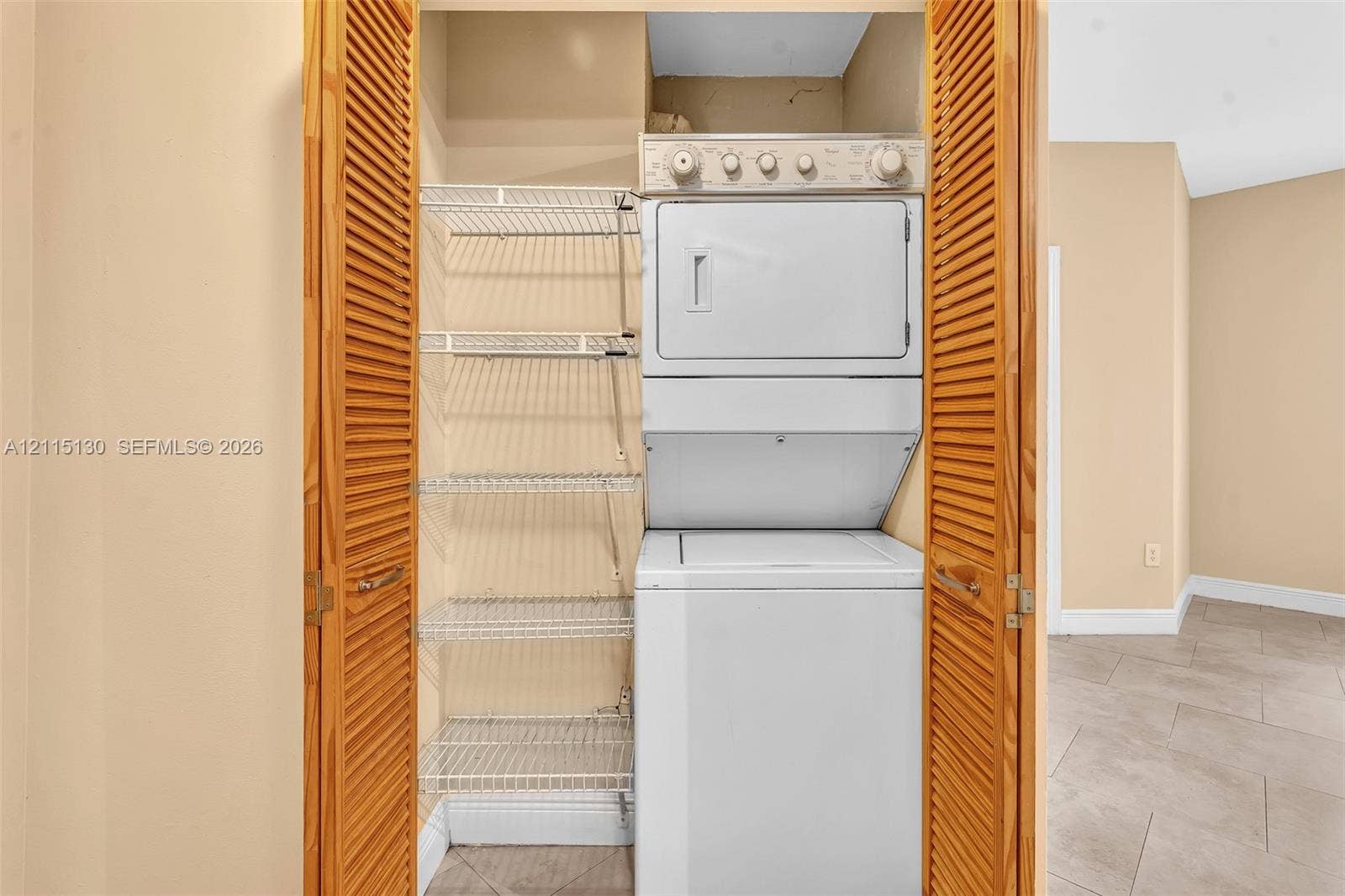 2445 SW 18th Terrace, #412, Fort Lauderdale, FL 33315 Laundry closet featuring louvered wooden doors, a stacked washer and dryer unit, and built-in wire shelving