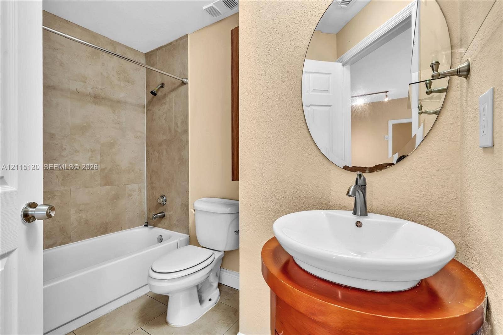 2445 SW 18th Terrace, #412, Fort Lauderdale, FL 33315 Oval wall-mounted mirror, vessel sink with brushed metal faucet, cylindrical wood-finish vanity, and shower-tub combination featuring tiled surround