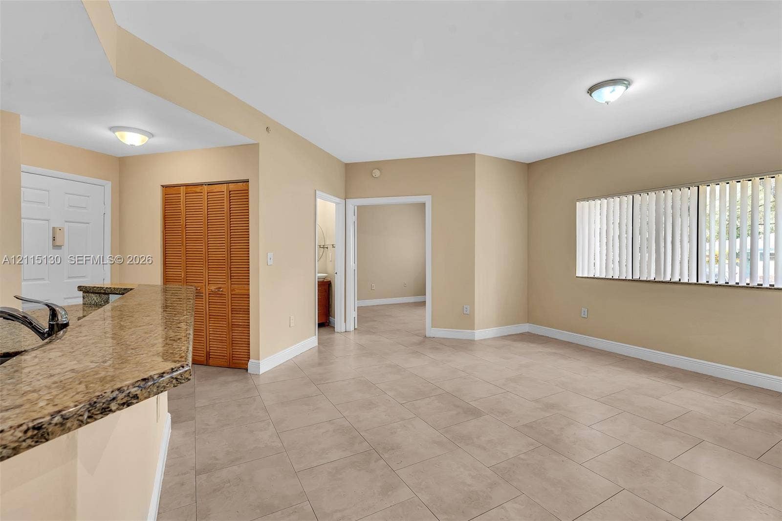 2445 SW 18th Terrace, #412, Fort Lauderdale, FL 33315 Open-concept interior featuring large-format ceramic tile flooring, kitchen breakfast bar with stone-finish countertop, dual flush-mount ceiling lights, and vertical blind window treatments