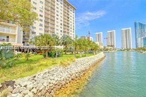 400 Kings Point Drive, #317, Sunny Isles Beach, FL 33160 Waterfront high-rise building featuring a stone-reinforced bulkhead, expansive landscaped grounds, and mature palm trees