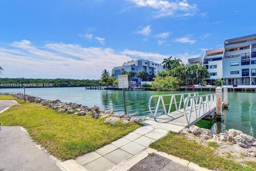 400 Kings Point Drive, #317, Sunny Isles Beach, FL 33160 Waterfront property featuring a metal gangway, stone-lined bulkhead, paved pathway, and grass landscaping