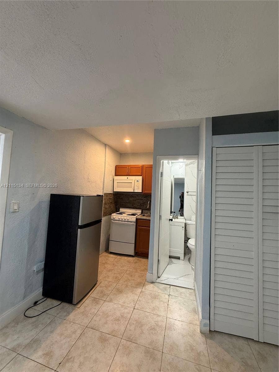2816 SW 4th Place, #B, Fort Lauderdale, Fort Lauderdale, FL 33312 Kitchen area featuring wood-finish cabinetry, a built-in over-the-range microwave, and light-toned floor tile, complete with a closet featuring louvered doors