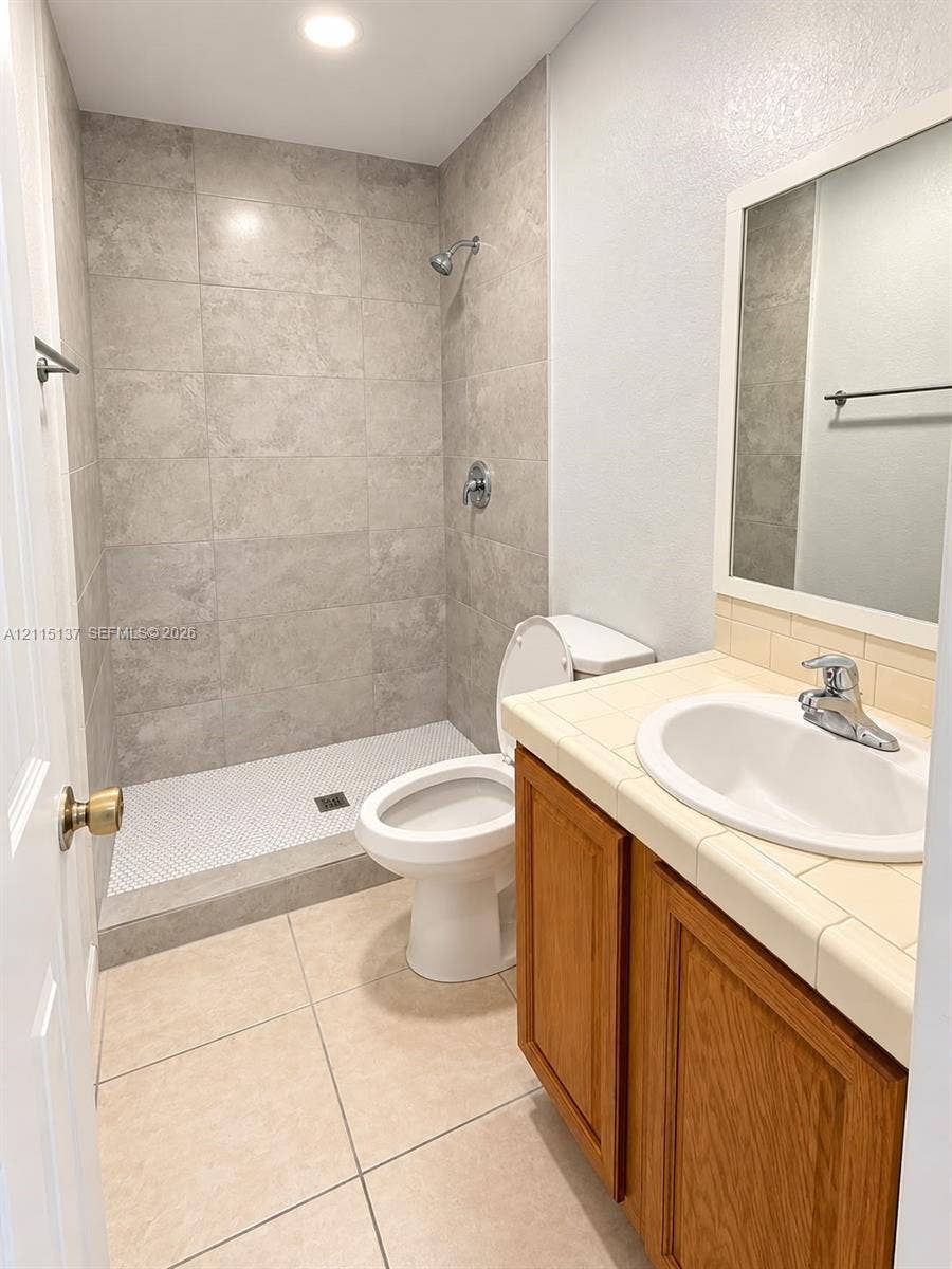 7870 SW 10th Court, #A, North Lauderdale, North Lauderdale, FL 33068 Bathroom featuring a walk-in shower with large-format wall tile and penny-tile flooring, wood-finish vanity with a tile countertop, recessed lighting, and a framed mirror