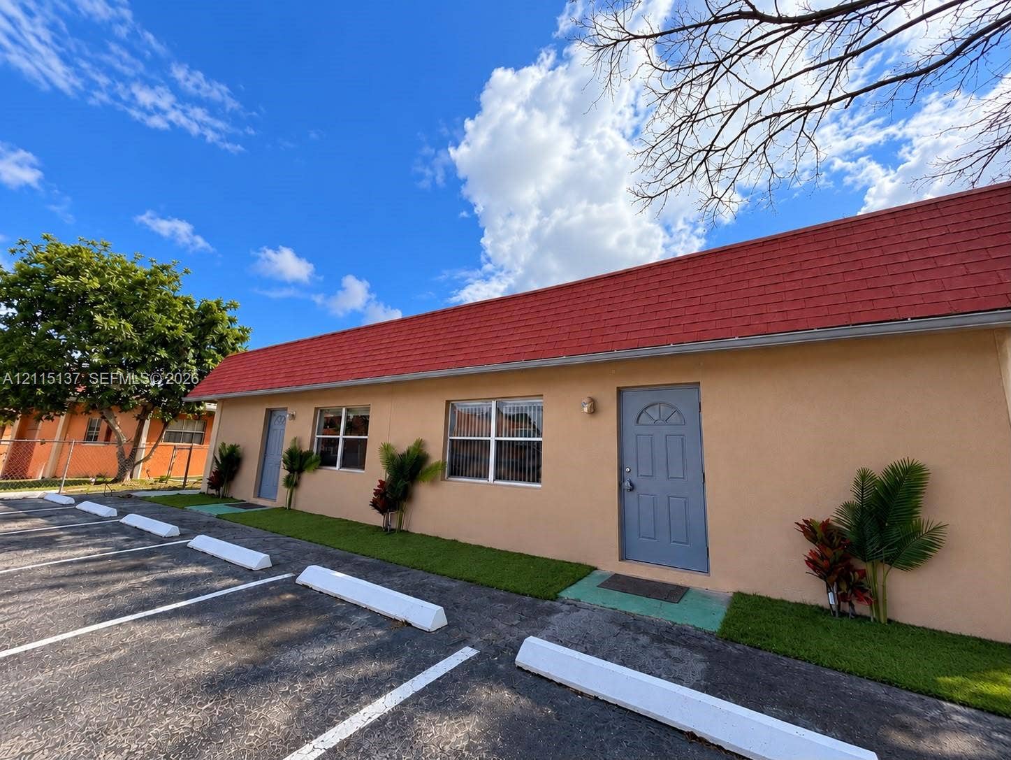 7870 SW 10th Court, #A, North Lauderdale, North Lauderdale, FL 33068 Single-story exterior featuring a red gable roof, stucco siding, and designated asphalt parking area with concrete bumpers