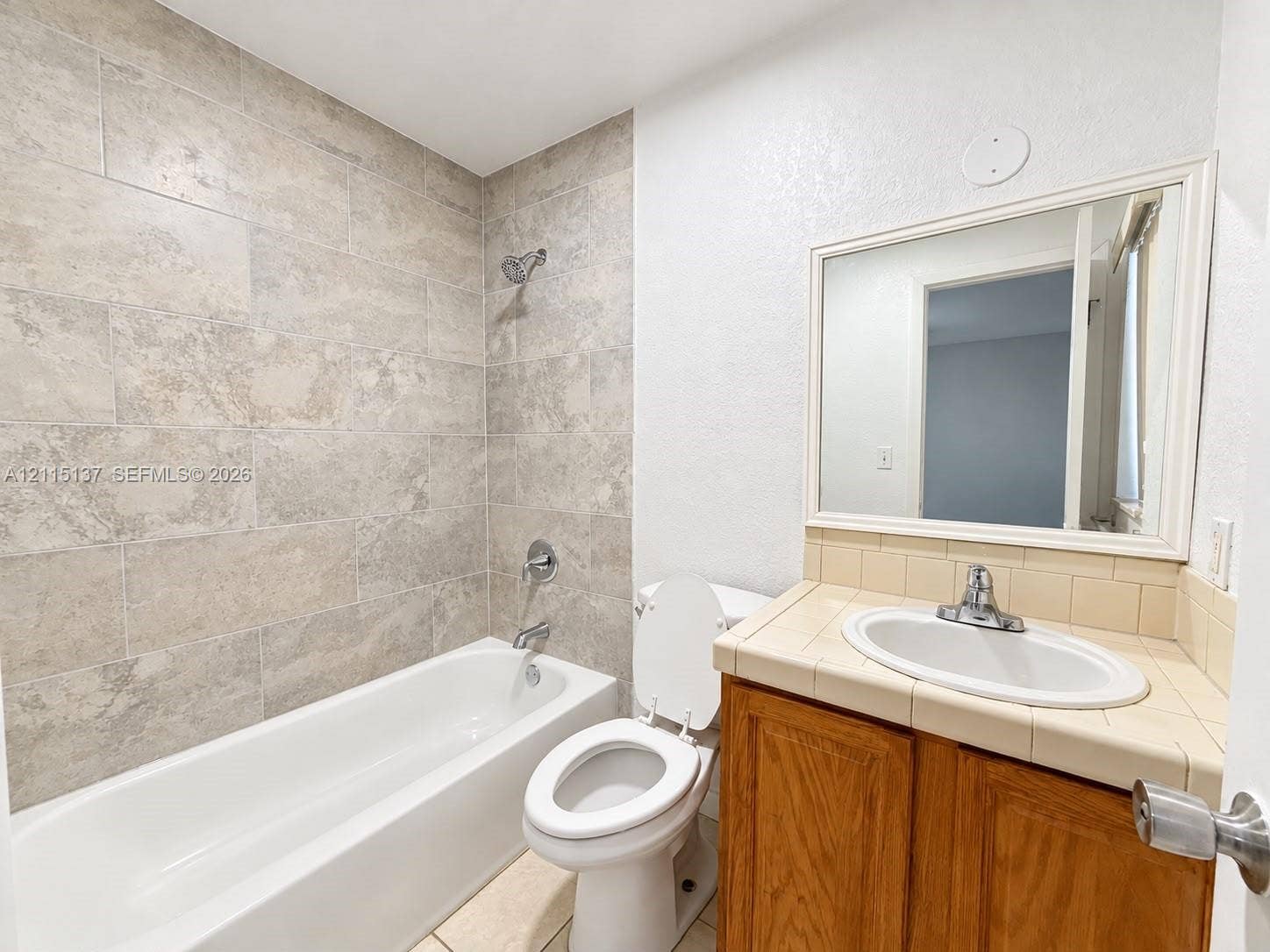 7870 SW 10th Court, #A, North Lauderdale, North Lauderdale, FL 33068 Bathroom featuring a tub-shower combination with large-format wall tile, wood-finish vanity cabinet with tile countertop, undermount sink, and framed wall-mounted mirror