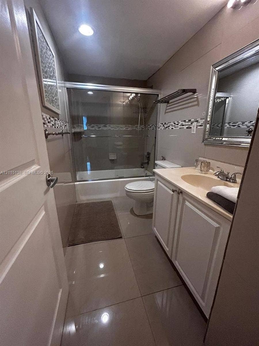 19380 Collins Avenue, #1602, Sunny Isles Beach, FL 33160 Full bathroom featuring a vanity with integrated sink, glass-enclosed shower and tub combination, neutral large-format floor tiling, and a mosaic tile backsplash