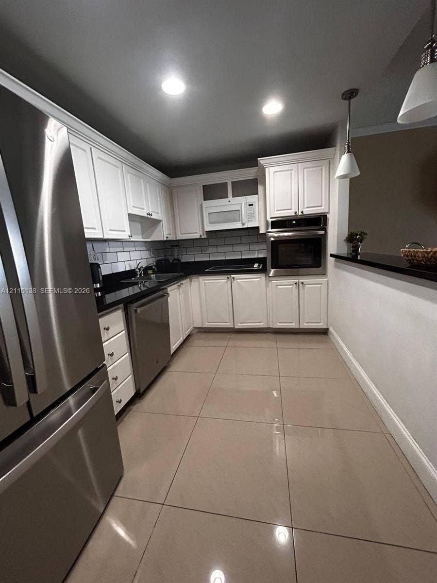19380 Collins Avenue, #1602, Sunny Isles Beach, FL 33160 Kitchen featuring white shaker-style cabinetry, dark stone countertops, subway tile backsplash, stainless steel appliances including a built-in wall oven, and large-format tile flooring