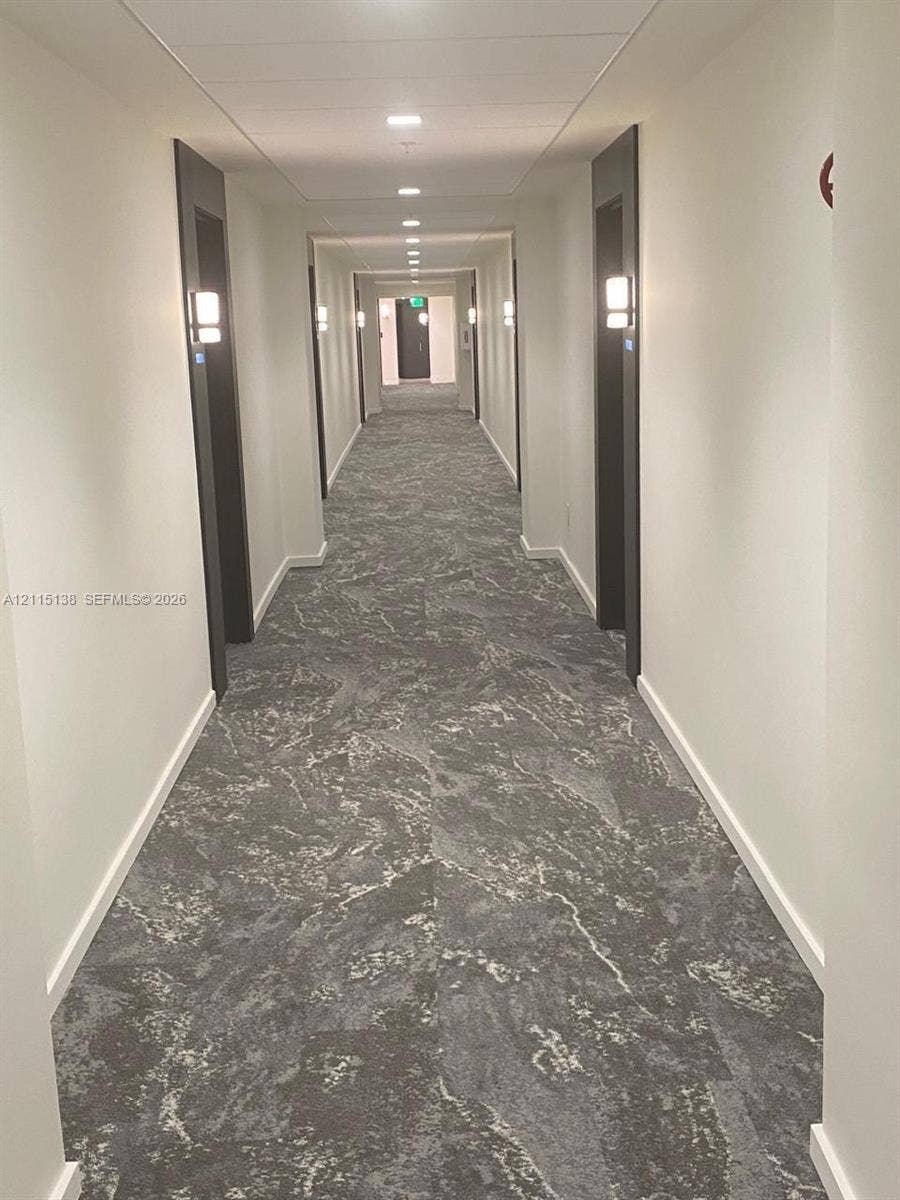 19380 Collins Avenue, #1602, Sunny Isles Beach, FL 33160 Hallway featuring patterned carpet flooring, recessed ceiling lighting, and wall-mounted light fixtures with dark door frames